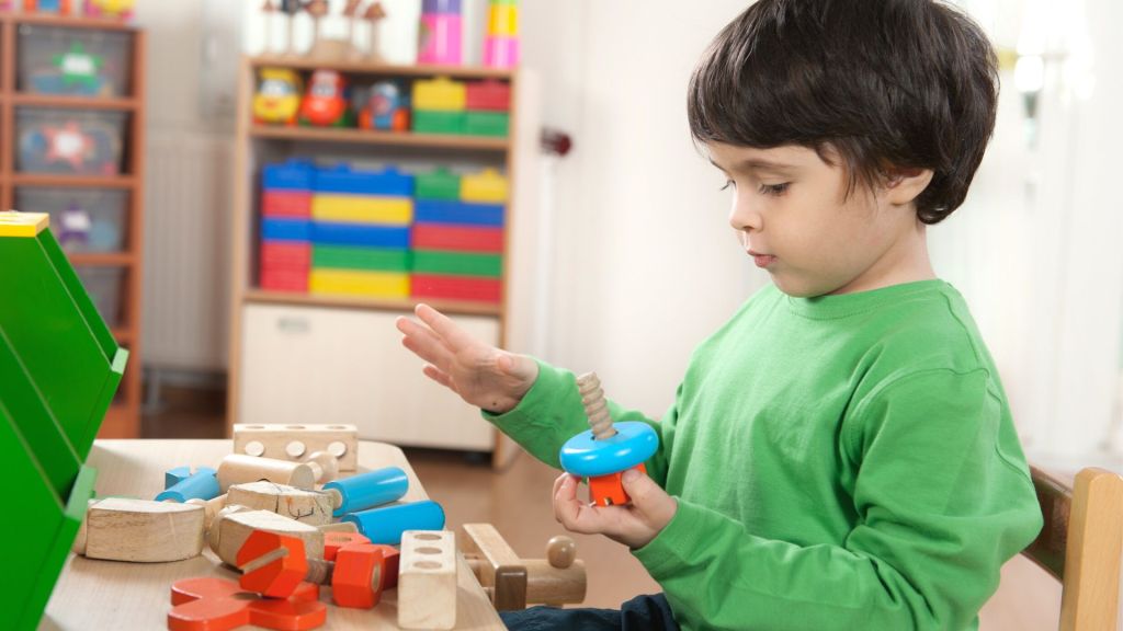 little boy plays with wooden building blocks in preschool